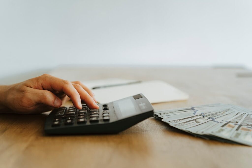 How a DSCR Loan Maine Can Help You Build Your Rental Empire 3 A person typing numbers into a calculator with hundred-dollar notes in front, checking to see if they meet the DSCR loan Maine requirements.