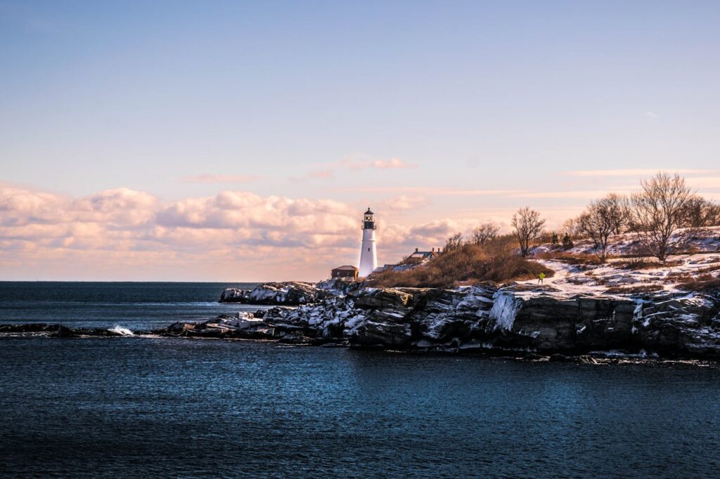 How a DSCR Loan Maine Can Help You Build Your Rental Empire 4 A lighthouse on the coast in Maine with snow covering the hills beside it.