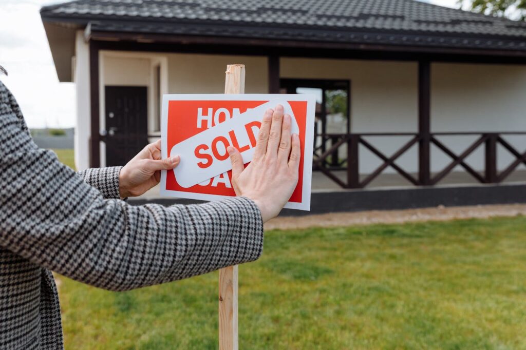 How to Prove Income When Self Employed to Get a Mortgage 1 A realtor is putting up a "sold" sign on a house after explaining to her clients how to prove income when self employed.