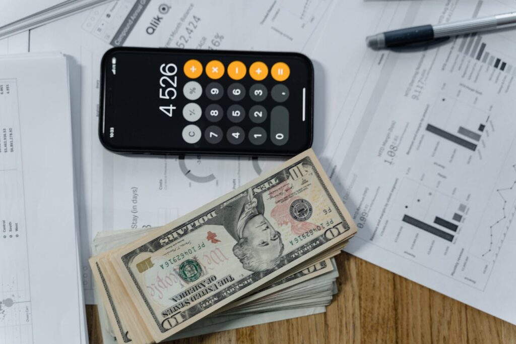 Your Guide to Asset Based Finance for Mortgages 1 A top-down view of a desk with investment statements, an iPhone calculator, and a stack of USD cash for a homebuyer considering asset based finance.